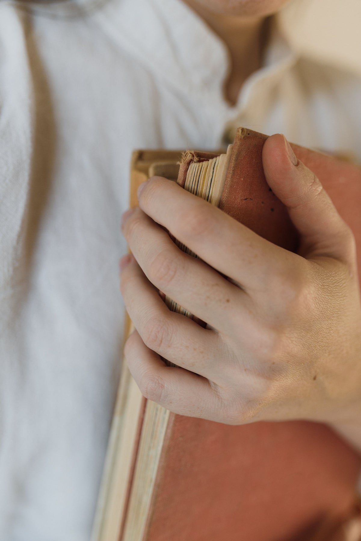 A hand holds a worn clothbound book, its aged page edges visible.